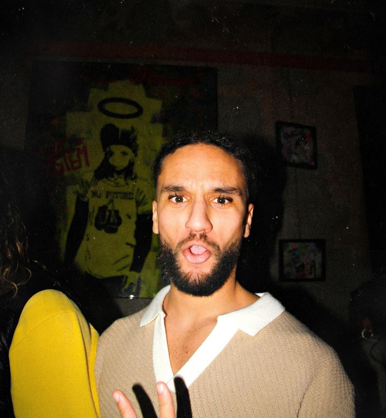 portrait nocturne d'un homme barbu expressif devant une toile street art, ambiance soirée d'une production vidéo brand content urbain south management
